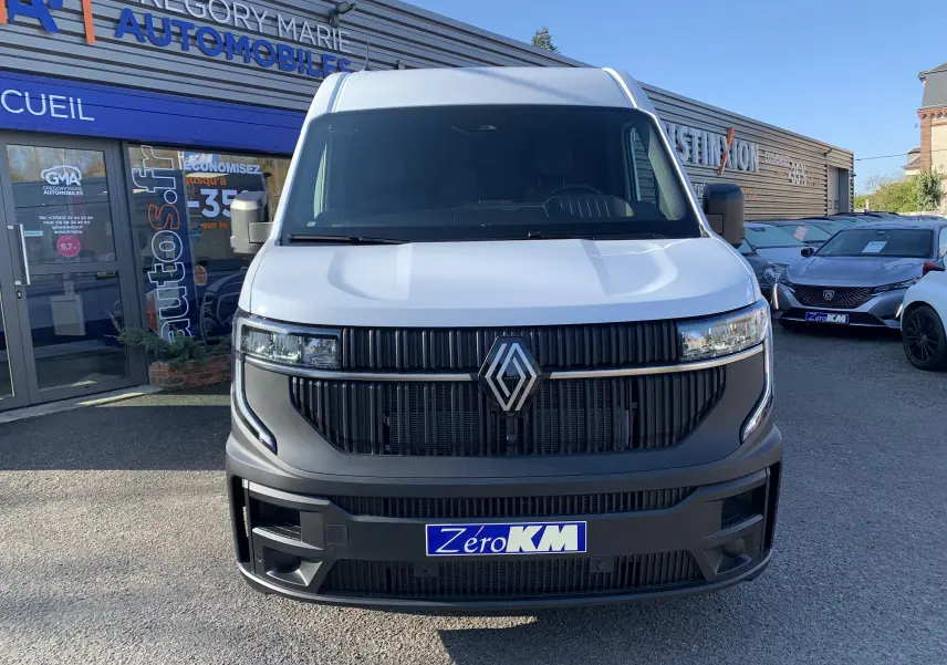 Vue avant d'un Renault Master blanc mine avec calandre noire et logo Renault proéminent, stationné devant un garage.