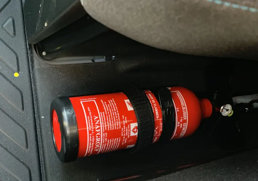 Extincteur rouge fixé au sol côté droit à l'avant d'un Renault Master blanc, visible dans l'habitacle près du siège passager.