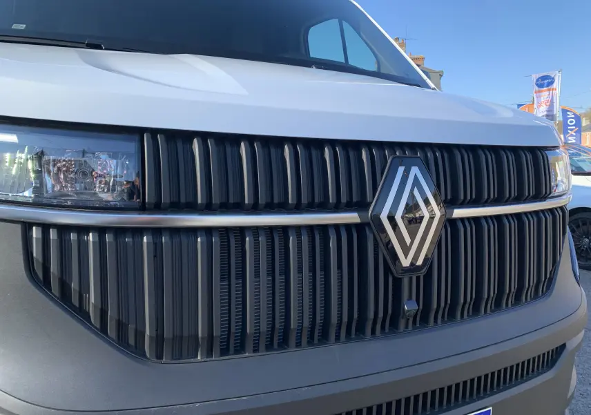 Gros plan sur la calandre noire et le logo Renault d’un Renault Master blanc mine, vue de face par temps clair.