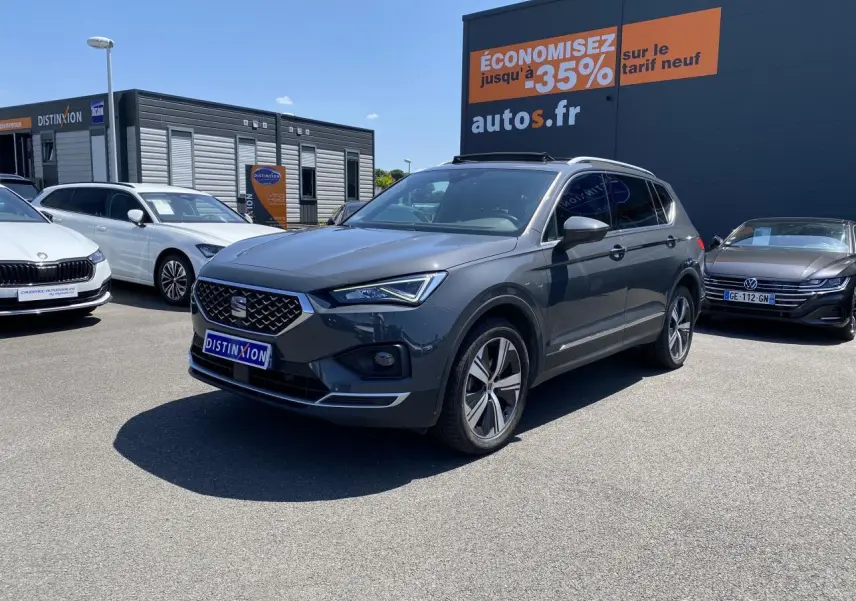 SEAT Tarraco gris dauphin vu en 3/4 avant droit sur un parking avec jantes alliage et toit panoramique.