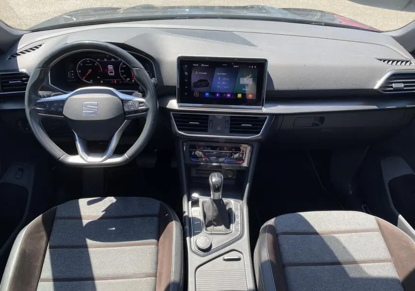 Vue intérieure frontale du tableau de bord du SEAT Tarraco 2022 avec volant multifonction et sellerie tissu gris à inserts bruns Alcantara.
