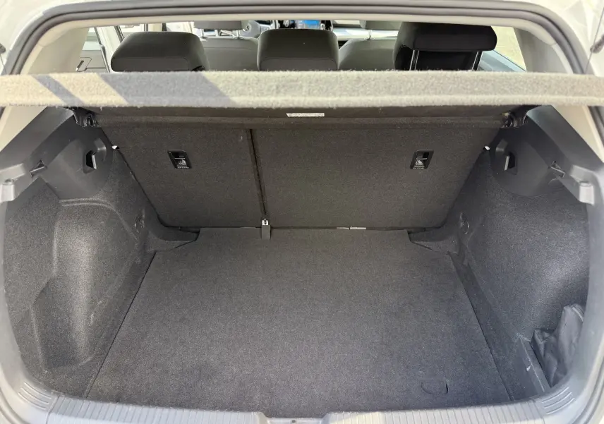 Coffre ouvert vu de l'arrière d'une Volkswagen Golf blanche 1.0 TSI 110 LIFE, intérieur noir et tapis de sol propre.
