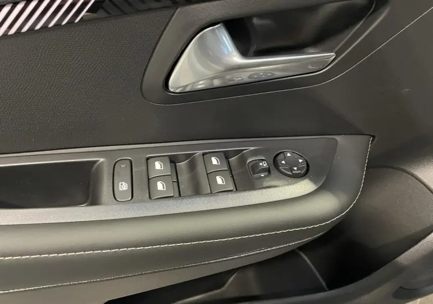Gros plan sur la commande des vitres et la poignée intérieure en chrome du panneau de porte avant gauche noir de Peugeot 208.