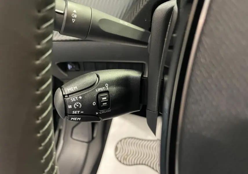 Gros plan sur la commande de régulateur de vitesse noire dans l'habitacle d'une Peugeot 208 hybride 2025.