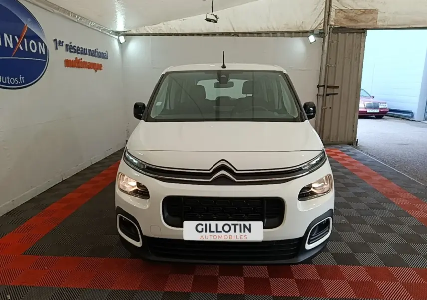 Vue avant d'un Citroën Berlingo blanc 2022 avec calandre noire et phares allumés en intérieur showroom.