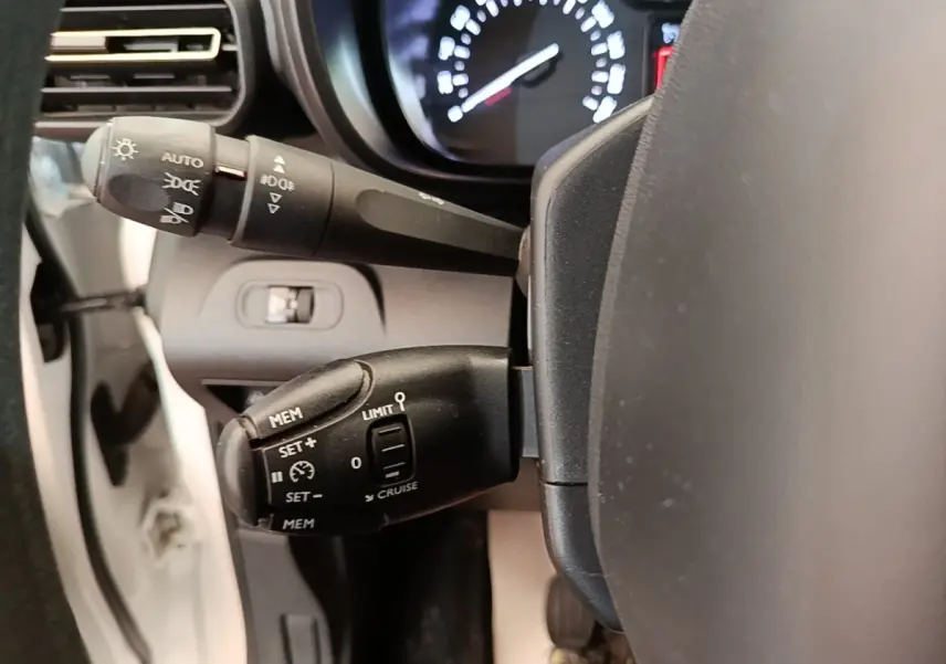 Gros plan sur les commandes de régulateur de vitesse du volant d'une Citroën Berlingo blanc, tableau de bord flou en arrière-plan.