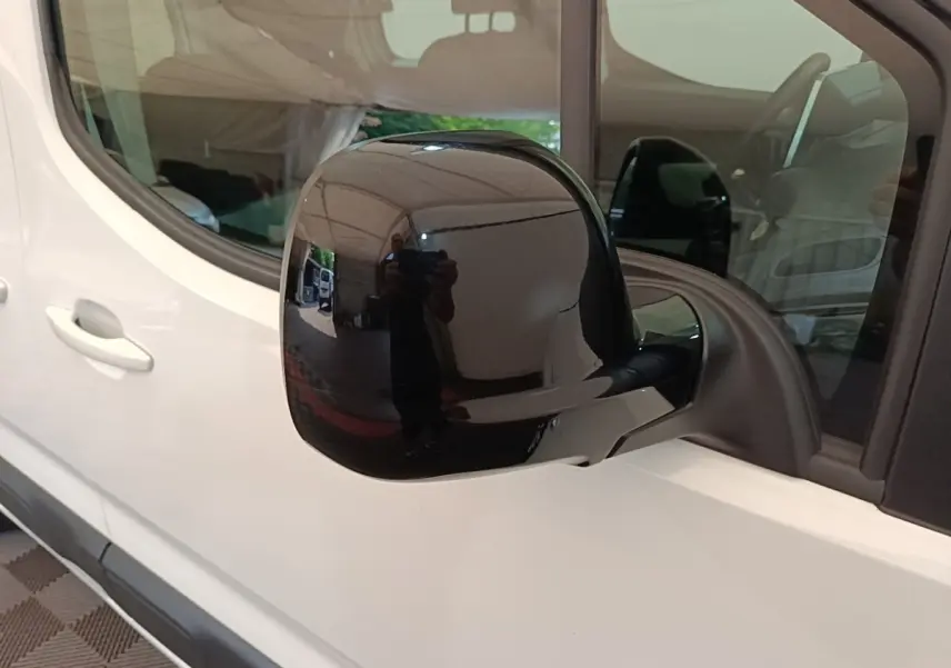 Rétroviseur noir en gros plan sur côté gauche d'un Citroën Berlingo blanc, vue latérale partielle.