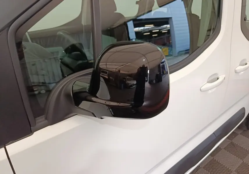 Rétroviseur noir en gros plan sur le côté gauche d’un Citroën Berlingo blanc, vue partielle latérale.