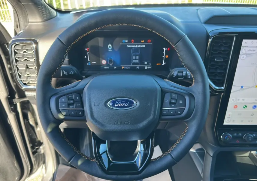 Vue rapprochée du volant cuir noir avec coutures marron et tableau de bord numérique du Ford Ranger gris carbone 2025.