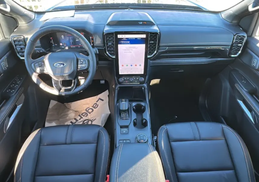 Vue intérieure du Ford Ranger 2025 Wildtrak Plus montrant le tableau de bord noir avec écran tactile vertical et volant multifonctions.
