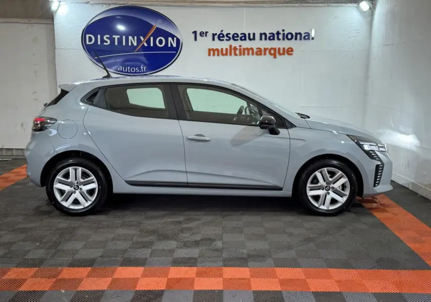 Profil droit d'une Renault Clio gris clair 2025 dans un showroom avec logo Distinxion en arrière-plan.
