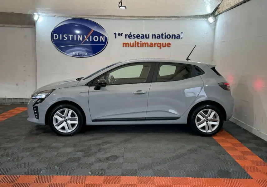 Profil droit d'une Renault Clio gris clair 2025 dans un showroom avec éclairage intérieur et sol noir et orange.