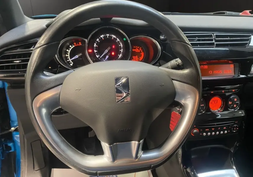 Vue intérieure centrée sur le volant alu et cuir d'une Citroën DS3 bleu, avec tableau de bord et commandes éclairées en rouge.