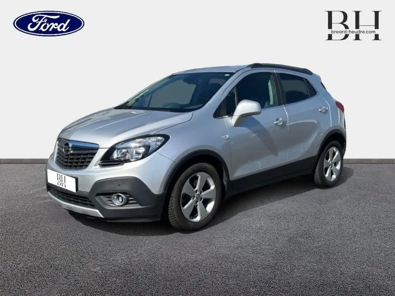 Opel Mokka gris minéral vue 3/4 avant droit avec jantes alliage et barres de toit noires.