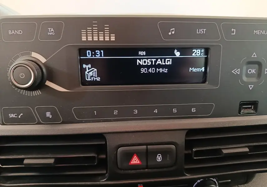 Vue rapprochée du tableau de bord du Peugeot Rifter blanc, affichant l'autoradio avec station Nostalgie à 90,40 MHz.