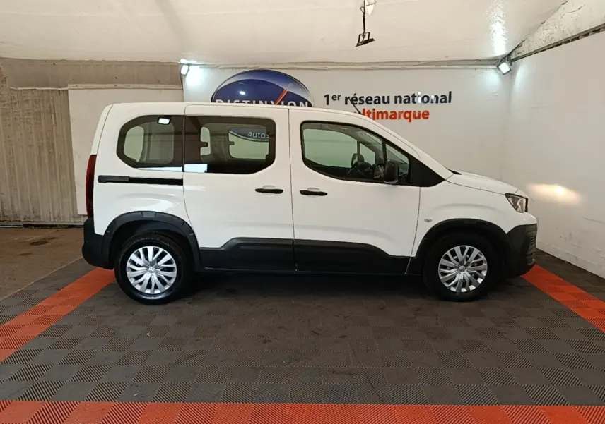 Vue de profil côté gauche d'un Peugeot Rifter blanc 2020 avec protections noires et jantes argentées en intérieur showroom.