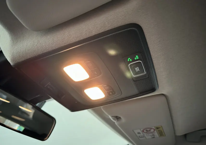 Plafonnier intérieur allumé avec bouton SOS vert sur Renault Clio gris clair, vue en contre-plongée depuis l'avant.