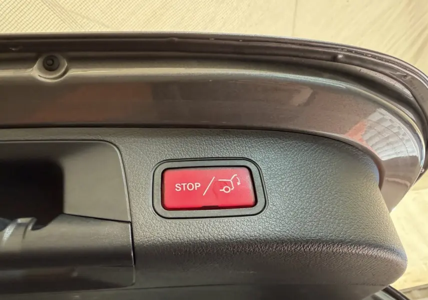 Bouton rouge stop ouverture coffre visible sur le bord intérieur du hayon gris clair d’un Mercedes GLA 250 e AMG Line 2023.