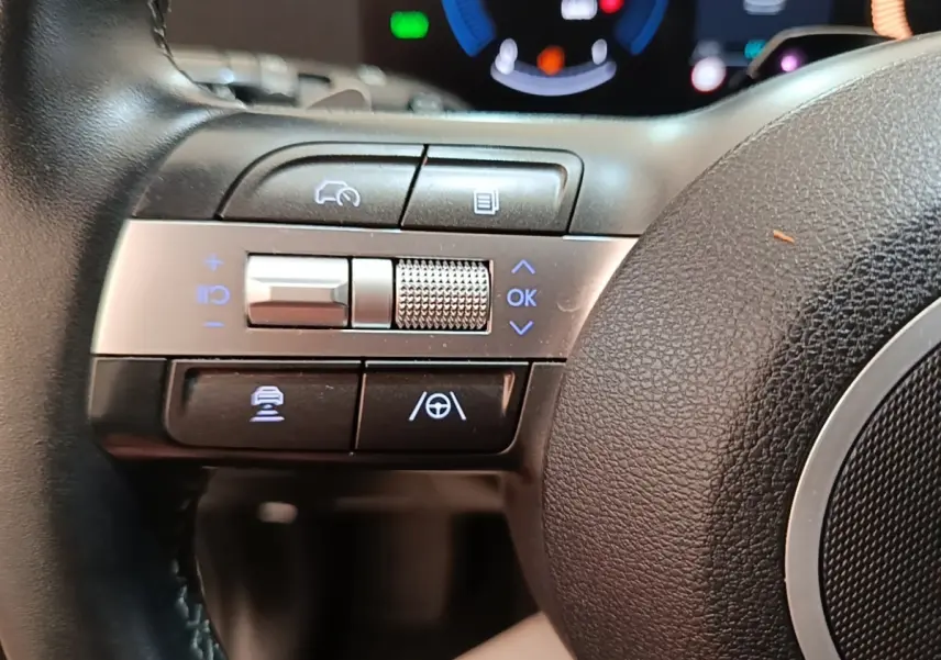Gros plan sur les commandes gauche du volant cuir du Hyundai Kona 1.6 Hybrid 2024, avec touches d’aide à la conduite.