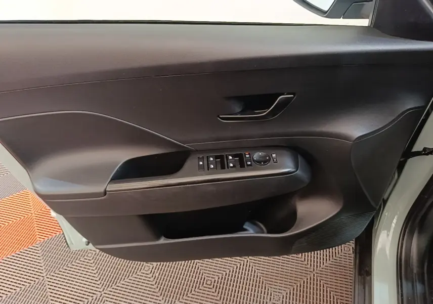 Vue intérieure de la porte avant gauche du Hyundai Kona 2024 vert, avec commandes électriques des vitres et rétroviseurs.