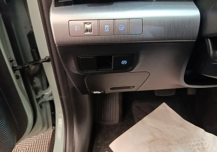 Détail des commandes sous le tableau de bord côté gauche du Hyundai Kona vert 2024, avec bouton frein à main électrique.