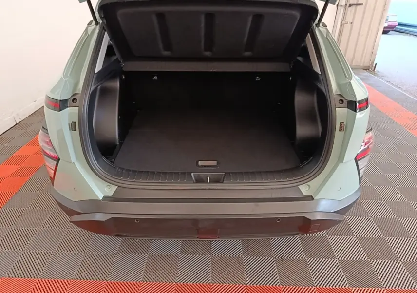 Vue arrière du coffre ouvert d'un Hyundai Kona 2024 vert, montrant l'espace de rangement vide et le pare-chocs noir.