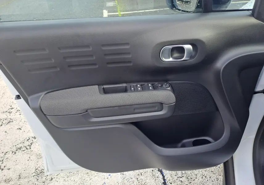Vue intérieure côté gauche de la porte avant blanche du Citroën C3 Aircross 2024 avec commandes électriques et accoudoir gris.