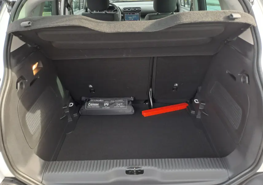 Coffre ouvert d'une Citroën C3 Aircross blanc banquise, montrant un triangle de signalisation rouge et une trousse de secours noire.