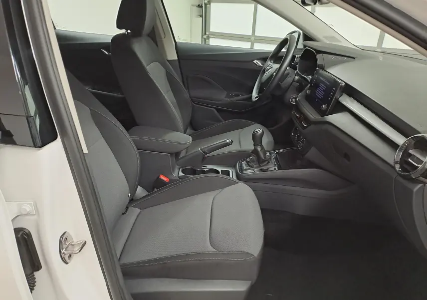 Intérieur côté conducteur d'une Skoda Fabia blanche 2023, avec sièges gris et tableau de bord moderne à écran tactile.