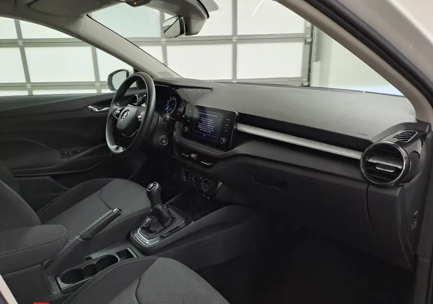 Intérieur côté conducteur de la Skoda Fabia 2023 blanc candy, tableau de bord moderne avec écran tactile et boîte manuelle.