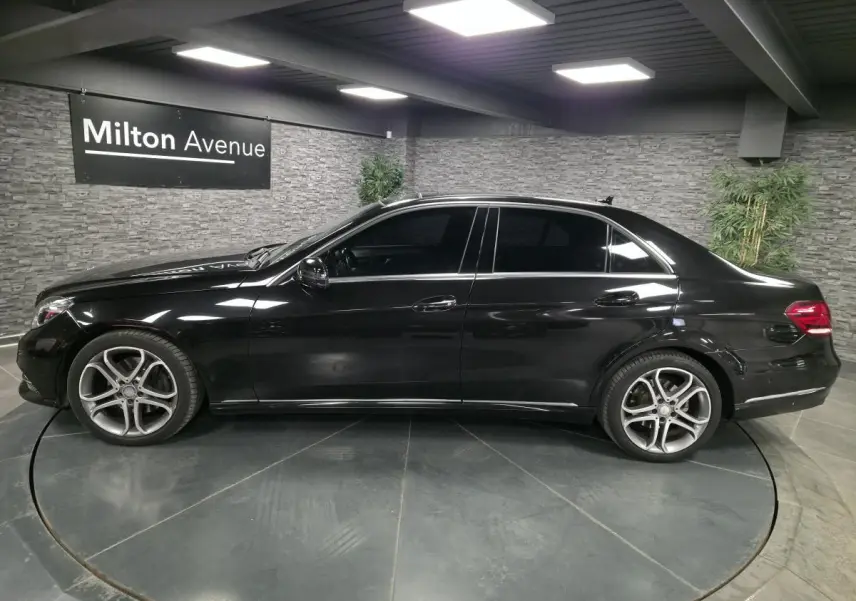 Profil côté gauche d'une Mercedes Classe E 300 BlueTEC Hybrid noire avec jantes alliage 18 pouces en intérieur showroom.