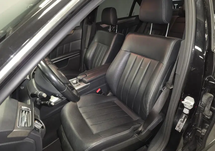 Intérieur noir de la Mercedes Classe E 300 BlueTEC Hybrid 2015, vue côté gauche sur sièges avant en cuir et tableau de bord.