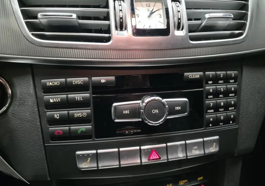Tableau de bord Mercedes Classe E 2015 noir, vue centrée sur console centrale avec horloge analogique et commandes multimédia.