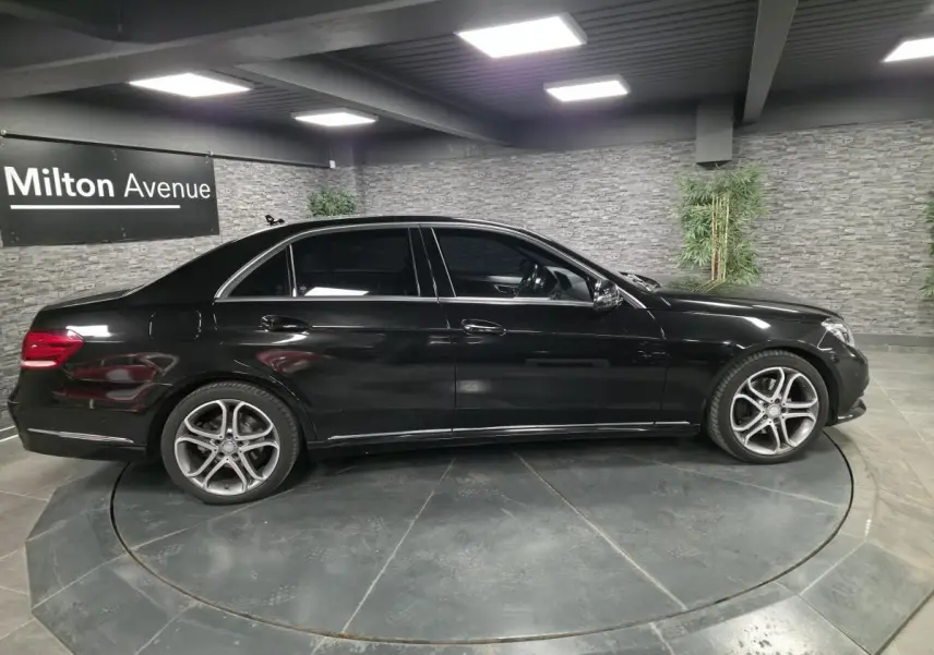 Profil droit d'une Mercedes Classe E noire de 2015 avec jantes alliage 18 pouces et vitres teintées dans un showroom.