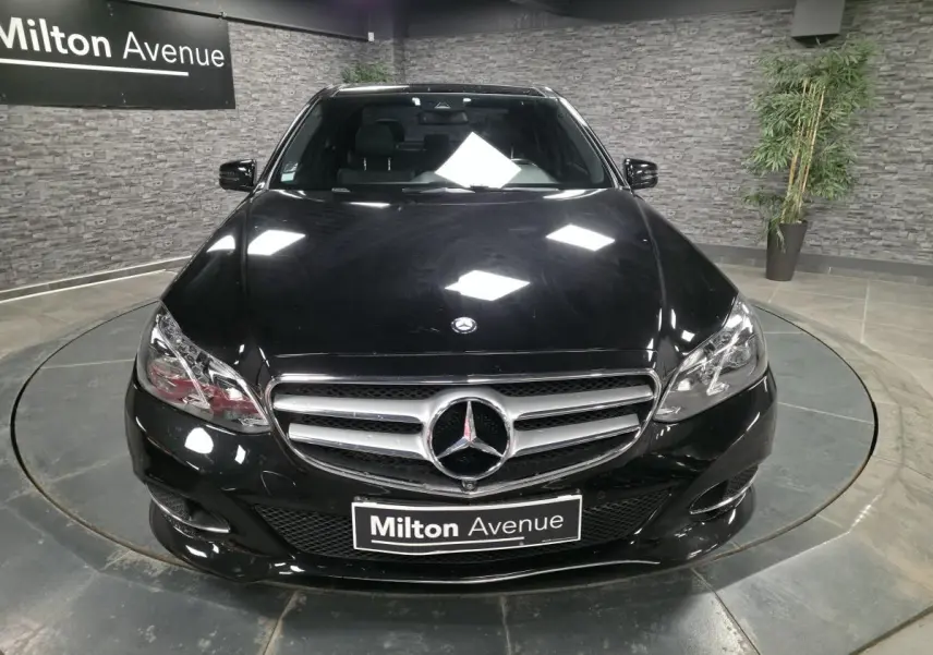 Vue avant d'une Mercedes Classe E noire avec calandre chromée et logo étoile centrale, en showroom intérieur.