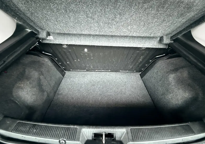 Coffre ouvert de la Fiat Punto 1.2 i 65 noire de 2009, montrant l’espace de rangement vide et la moquette grise.