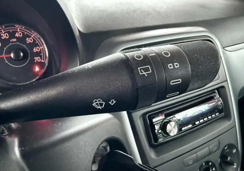 Gros plan sur la commande d’essuie-glace noire dans l’habitacle d’une Fiat Punto 2009, avec tableau de bord et autoradio en arrière-plan.