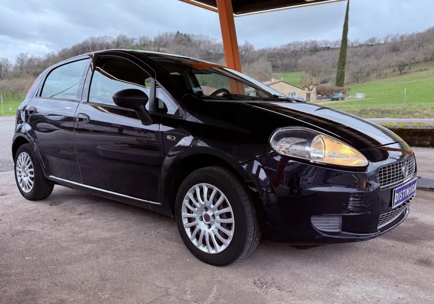 Vue 3/4 avant droite d'une Fiat Punto noire de 2009 avec phares allumés et jantes multibranches sous abri.