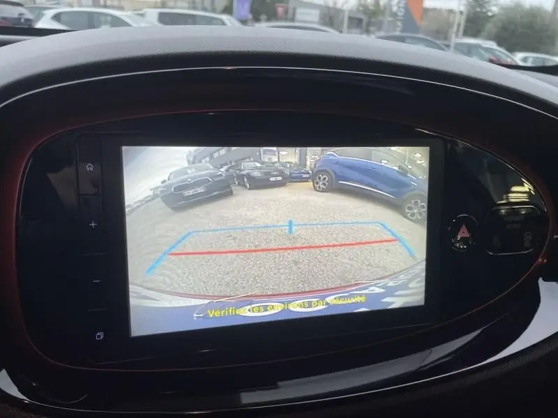 Vue arrière en caméra de recul de la Toyota Aygo X rouge piment avec toit noir, montrant le stationnement et les lignes d’aide au recul.