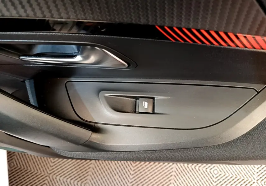 Détail de la porte côté conducteur d’une Peugeot 2008 blanche, avec bouton de commande de vitre et insert décoratif rouge.