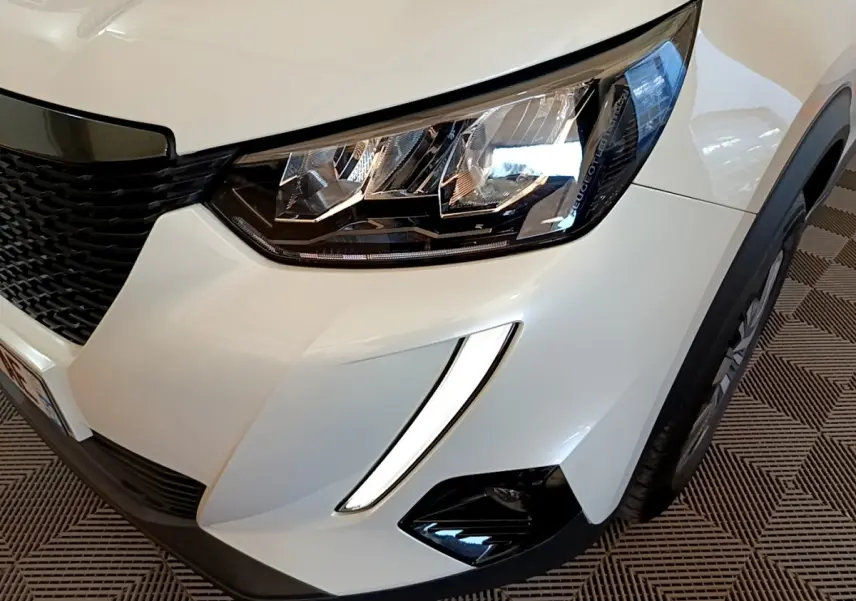Gros plan sur l'avant droit blanc du Peugeot 2008 2021, mettant en valeur le phare LED et la grille noire.