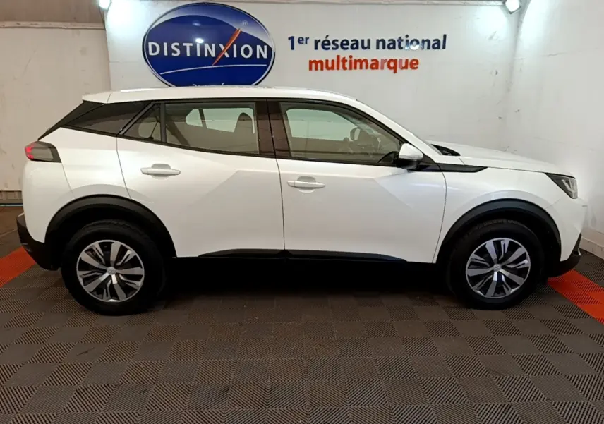 Vue de profil côté gauche d’un Peugeot 2008 blanc 2021, avec jantes alliage et toit noir contrasté en intérieur showroom.
