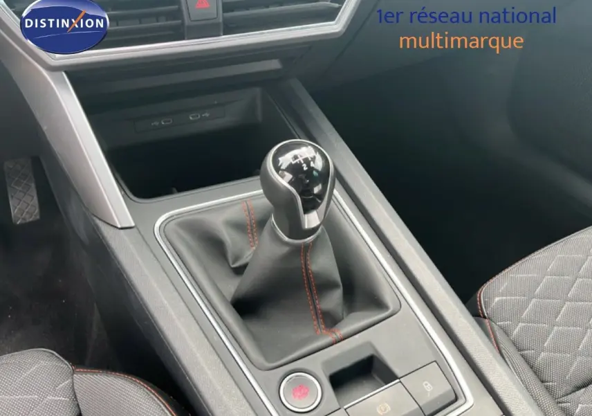 Gros plan sur la console centrale avec levier de vitesse manuel et surpiqûres rouges, siège tissu gris noir visible.