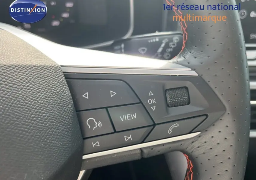 Gros plan sur les commandes du volant perforé avec surpiqûres rouges d'une SEAT LEON ST gris magnétique 2025.