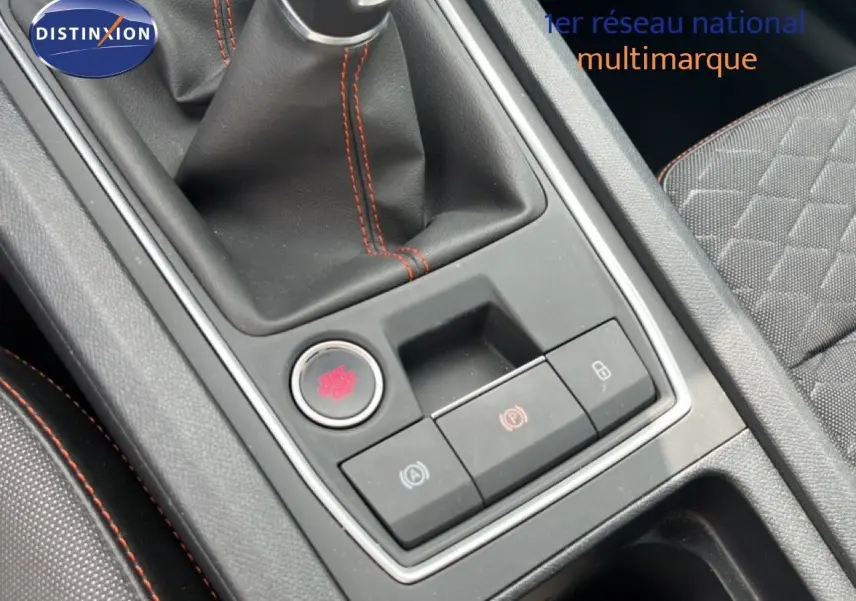 Gros plan sur la console centrale de la SEAT LEON ST 2025, avec levier de vitesse manuel et surpiqûres rouges.