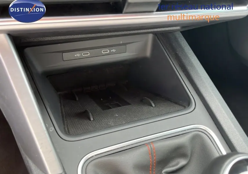 Gros plan sur la console centrale de la SEAT LEON ST 2025, montrant le rangement avec ports USB et soufflet de levier de vitesse noir.