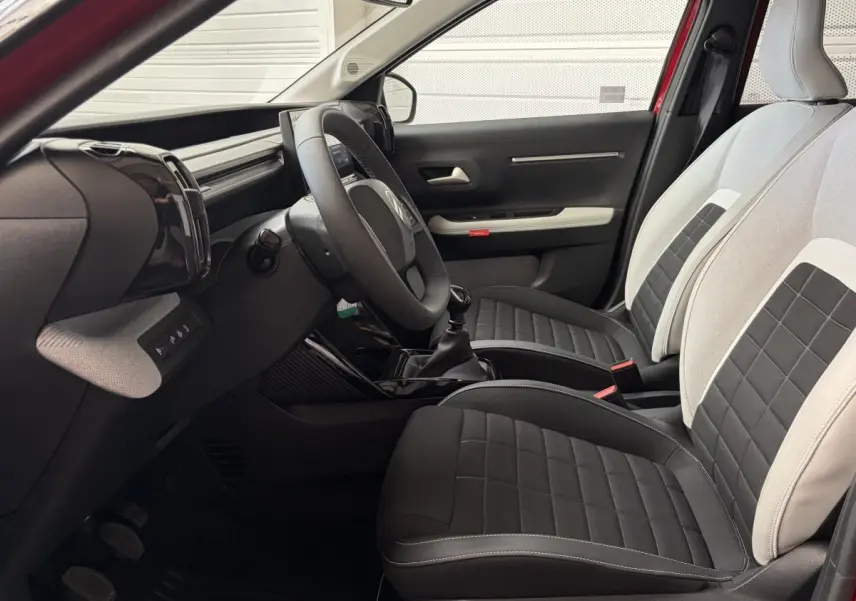Vue intérieure côté conducteur de la Citroën C3 2025, sièges bi-ton noir et beige avec volant cuir et boîte manuelle.