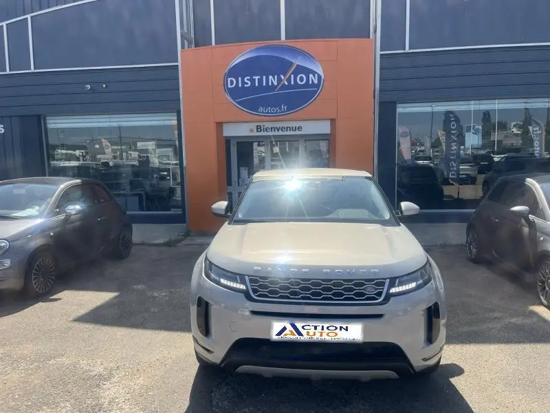 Vue frontale d'un Range Rover Evoque Indus Silver 2019 stationné devant un garage avec logo Distinxion.