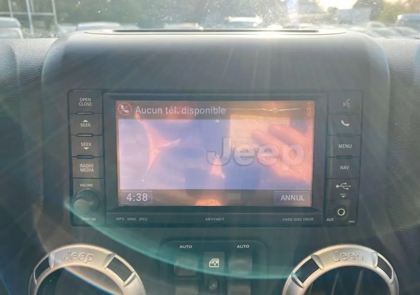 Détail de l'écran multimédia et des aérateurs marqués Jeep dans l'habitacle d'un Wrangler gris clair 2012.