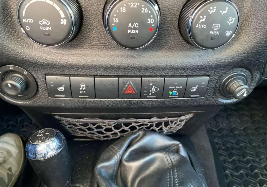 Gros plan sur la console centrale du Jeep Wrangler 2012 gris clair, montrant la boîte manuelle et les commandes de climatisation.